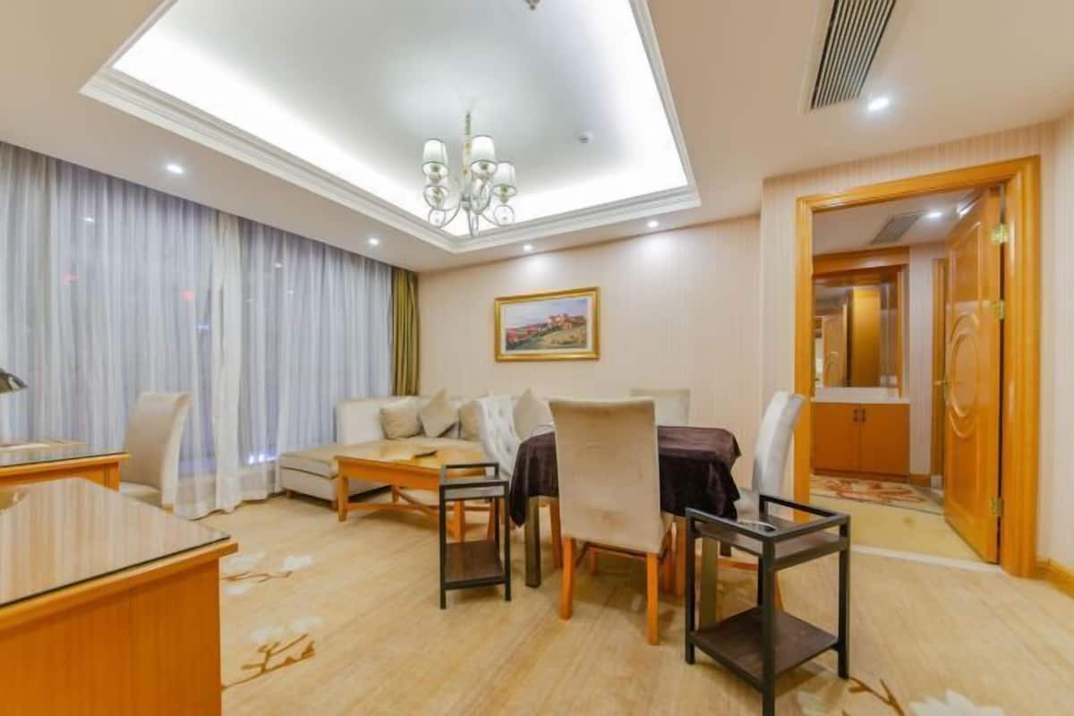 A hotel room with a dining area, a sofa set, a desk, and a chandelier.