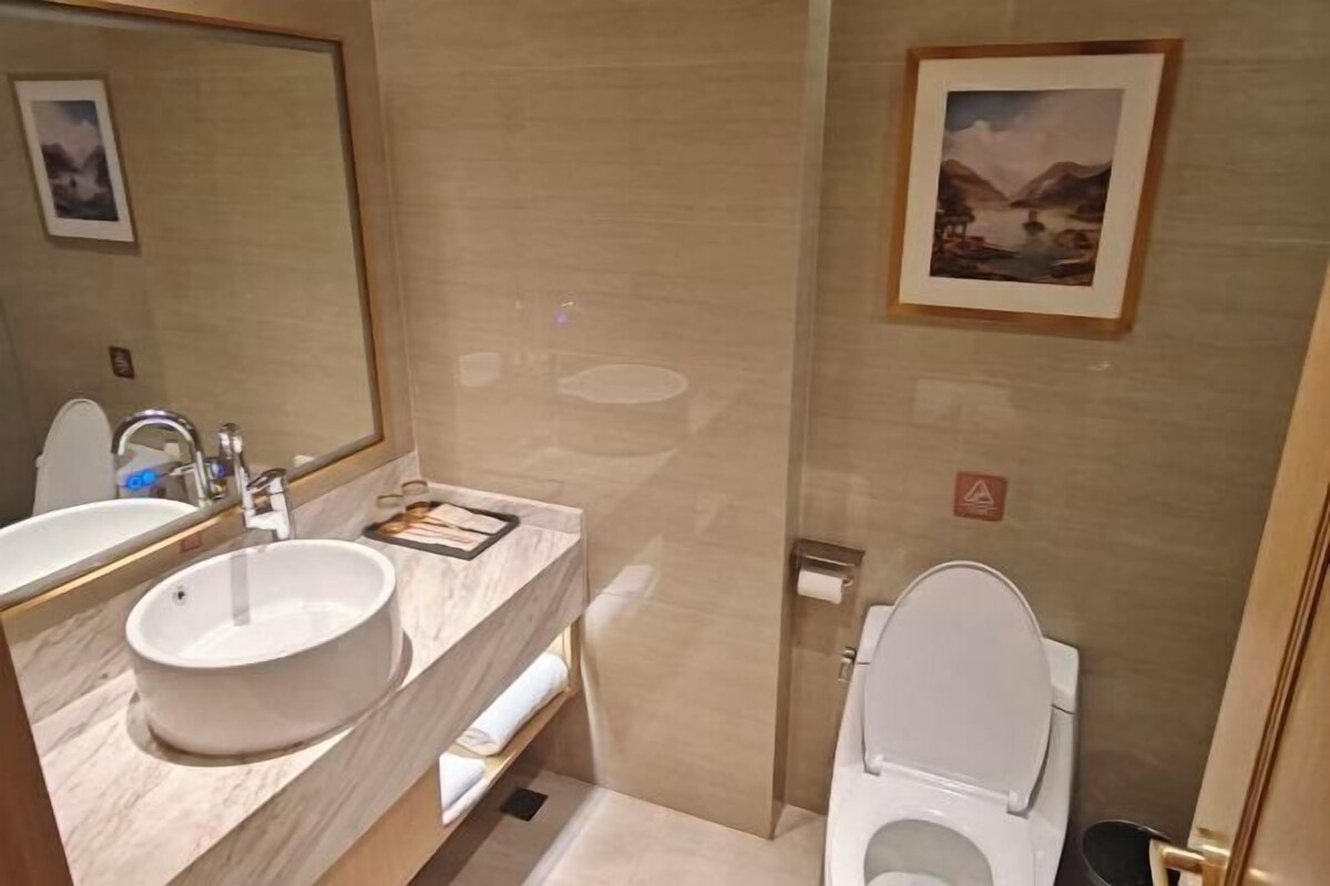 A bathroom with a sink, mirror, toilet, and a framed picture on the wall.