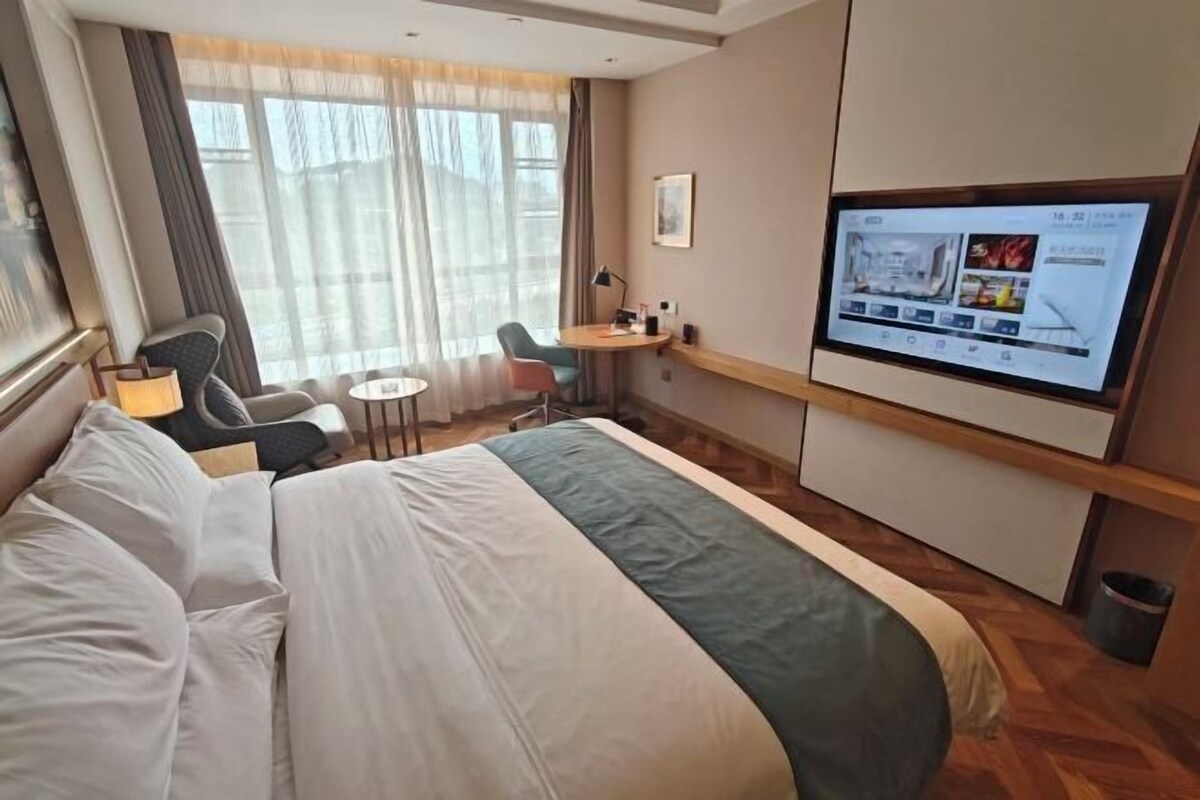 A hotel room with a bed, a desk, a chair, a television, and a window with curtains.