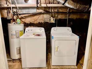 Une buanderie équipée d’un chauffe-eau, de deux machines à laver et dont la tuyauterie est visible.