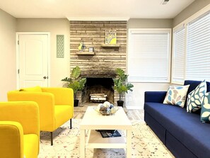 A living room with a fireplace, yellow and blue sofas, and a coffee table. - Vibrant 3BR Greensboro Home | Game Room & Yard (Greensboro)