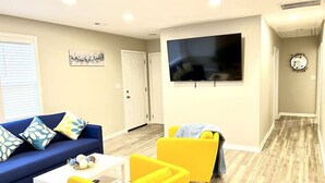 A living room with a blue sofa, yellow armchairs, a flat-screen TV, and a wooden floor.
