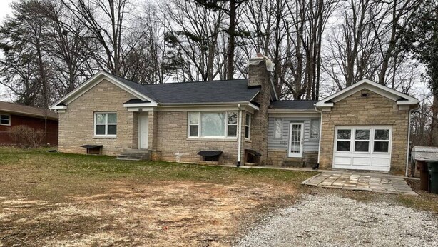 A two-story house with a front porch, a garage, and a gravel driveway.