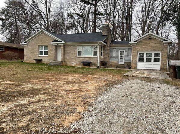 A two-story house with a front porch, a garage, and a gravel driveway.
