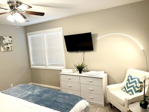 Une chambre à coucher comprenant un lit, une commode, une chaise, un téléviseur et un ventilateur de plafond.