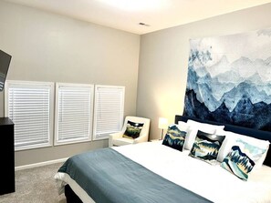 Une chambre à coucher avec un lit, une chaise, un grand tableau et une fenêtre avec des stores.