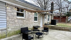 En udendørs patio med fire sorte stole og et rundt bord, en stenvæg og en skorsten.