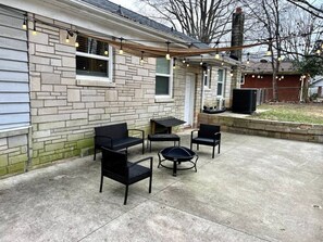Une terrasse extérieure avec quatre chaises noires et une table ronde, un mur en pierre et une cheminée.