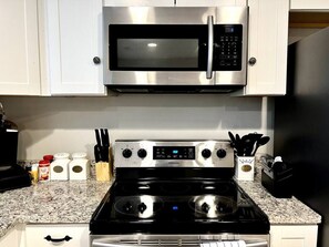Une cuisine équipée d’un four à micro-ondes en acier inoxydable, d’une cuisinière à quatre brûleurs et d’une horloge numérique.
