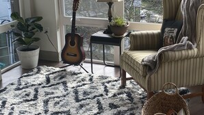 A cozy room with a large window, a guitar, a lamp, a potted plant, a striped armchair, and a woven basket. - Enjoy Seattle with comfort and style! (Seattle)