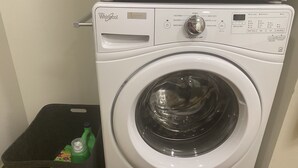 A front-loading Whirlpool washer with a control panel, a grey laundry basket, and a green bottle of laundry detergent. - Enjoy Seattle with comfort and style! (Seattle)