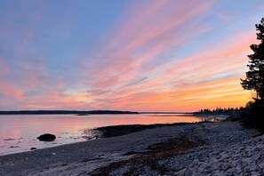 En strand med en stenig kustlinje och stilla vatten som speglar himlen.