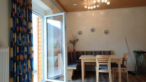 Une pièce avec un plafond en bois, une table à manger avec des chaises, un banc et une porte-fenêtre coulissante.