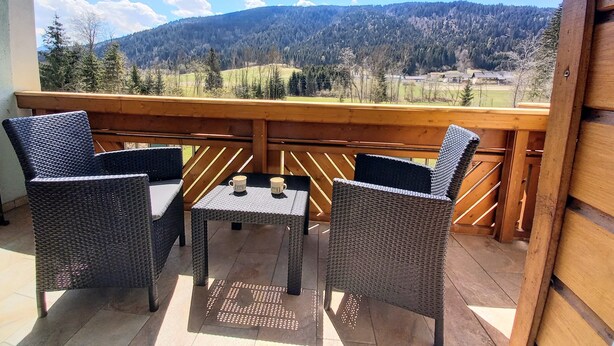 Un balcon doté de meubles en osier et d’une table, offrant une vue sur un paysage montagneux.