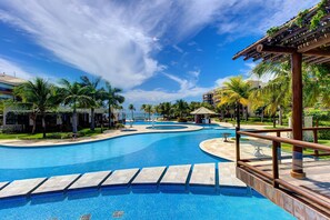 Piscina com design curvo, cercada por palmeiras e um céu claro.