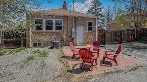 Una piccola casa in mattoni con un patio arredato con sedie rosse e un tavolo.