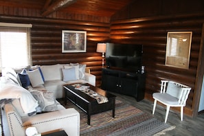A log cabin interior with a sofa, coffee table, TV, and a chair. - Log home just 32 miles to the east gate of Yellowstone National Park (Cody)