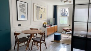 A modern living room with a round wooden table, two chairs, a TV, and artwork on the wall. - Contemporary Urban Apartment (London)