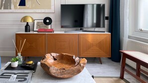 A modern living room with a wooden cabinet, a flat-screen TV, a decorative bowl, and a magazine on the coffee table. - Contemporary Urban Apartment (London)