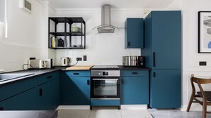 A modern kitchen with teal cabinets, a built-in oven, and a coffee maker. - Contemporary Urban Apartment (London)
