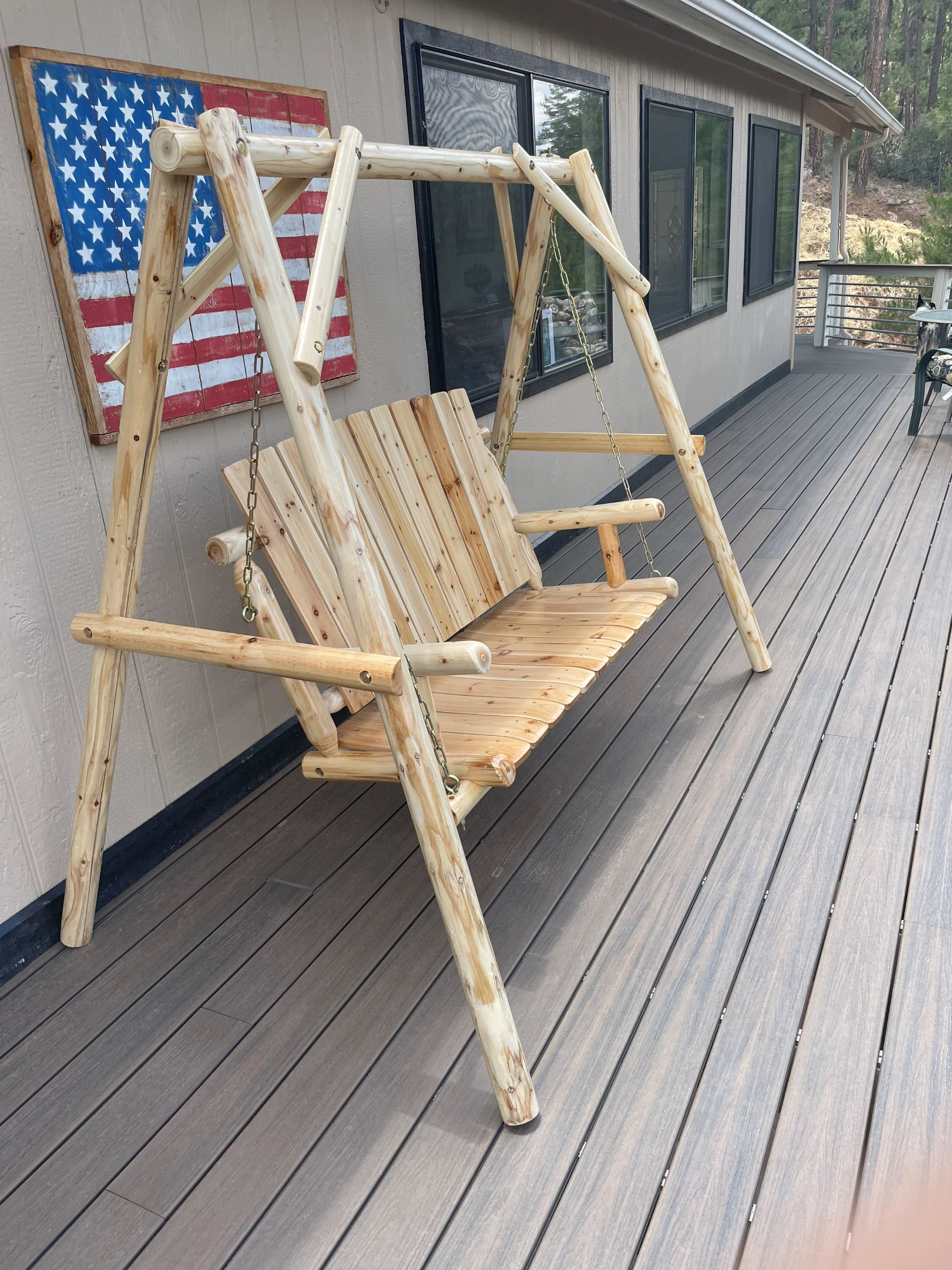 Una silla mecedora de madera con respaldo y apoyabrazos, hecha con troncos, sobre una terraza de madera.
