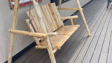 Una silla mecedora de madera con respaldo y apoyabrazos, hecha con troncos, sobre una terraza de madera.