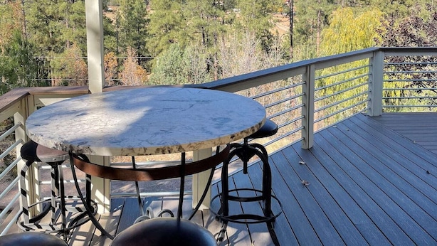 Una terraza techada al aire libre con una mesa redonda y dos taburetes, con vistas a un paisaje montañoso.