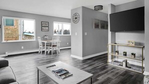 Un salon moderne comprenant un coin repas, des murs gris, un grand téléviseur et une cheminée.