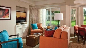 Een ruime woonkamer met een groot raam, een televisie en een eethoek met rode stoelen.