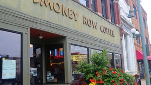 The exterior of Smokey Row Coffee, featuring large windows, a brick facade, and a planter with flowers in front.