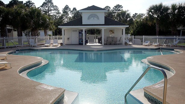 A swimming pool with a gazebo, lounge chairs, and a fenced area. - Palm Cove Paradise (Panama City Beach)