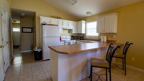 A kitchen with white cabinets, a central island with two chairs, a refrigerator, microwave, and a sink. - Palm Cove Paradise (Panama City Beach)
