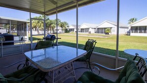 A covered patio with a glass table and chairs, overlooking a lawn with houses in the background. - Palm Cove Paradise (Panama City Beach)