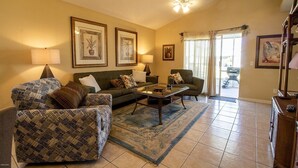 A living room with a sofa, armchair, and coffee table, a chandelier, and framed artwork on the walls. - Palm Cove Paradise (Panama City Beach)