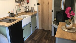A compact kitchen with a dishwasher, sink, wooden cabinets, a stove, and a small dining table with a vase of flowers. - Wyncliffe Hideaway (Haverfordwest)
