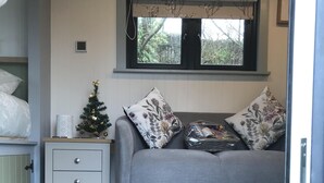 A living room with a grey sofa, floral cushions, a small Christmas tree, and a rug with "Merry & Bright" text. - Wyncliffe Hideaway (Haverfordwest)