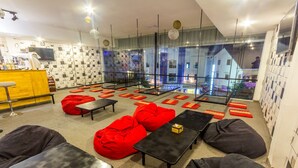 A modern lounge area with red bean bags, black tables, and a yellow bar counter. - Oasis Capsules - Hostel (Siem Reap)