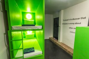 A bunk bed room with green lighting, a wall with a quote, and a door in the background. - Oasis Capsules - Hostel (Siem Reap)