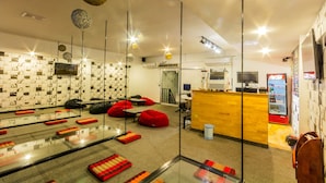 A modern hotel lobby with a reception desk, seating area with red bean bags, and a wall with patterned tiles. - Oasis Capsules - Hostel (Siem Reap)