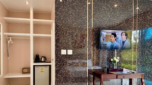 A hotel reception area with a marble wall, a television displaying 'The Good Doctor', a small fridge, and a wooden desk with a vase.