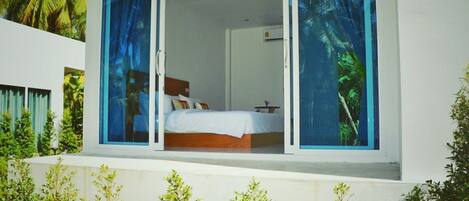 Un dormitorio con cama, mesita de noche y ventana con vista a palmeras.
