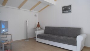 Ein Wohnzimmer mit einem weißen Sofa, einem Fernseher auf einem Schrank, einer hohen Lampe und einem kleinen Tisch mit einem dekorativen Gegenstand.