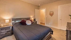 A bedroom with a large bed, a nightstand with a lamp, a wall-mounted light fixture, and a door with a decorative hanging. - Mountain Views Newly Renovated Home (Ogden)
