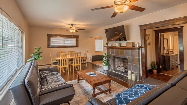 A living room with a fireplace, ceiling fans, a sofa, a coffee table, and a dining area. - Mountain Views Newly Renovated Home (Ogden)