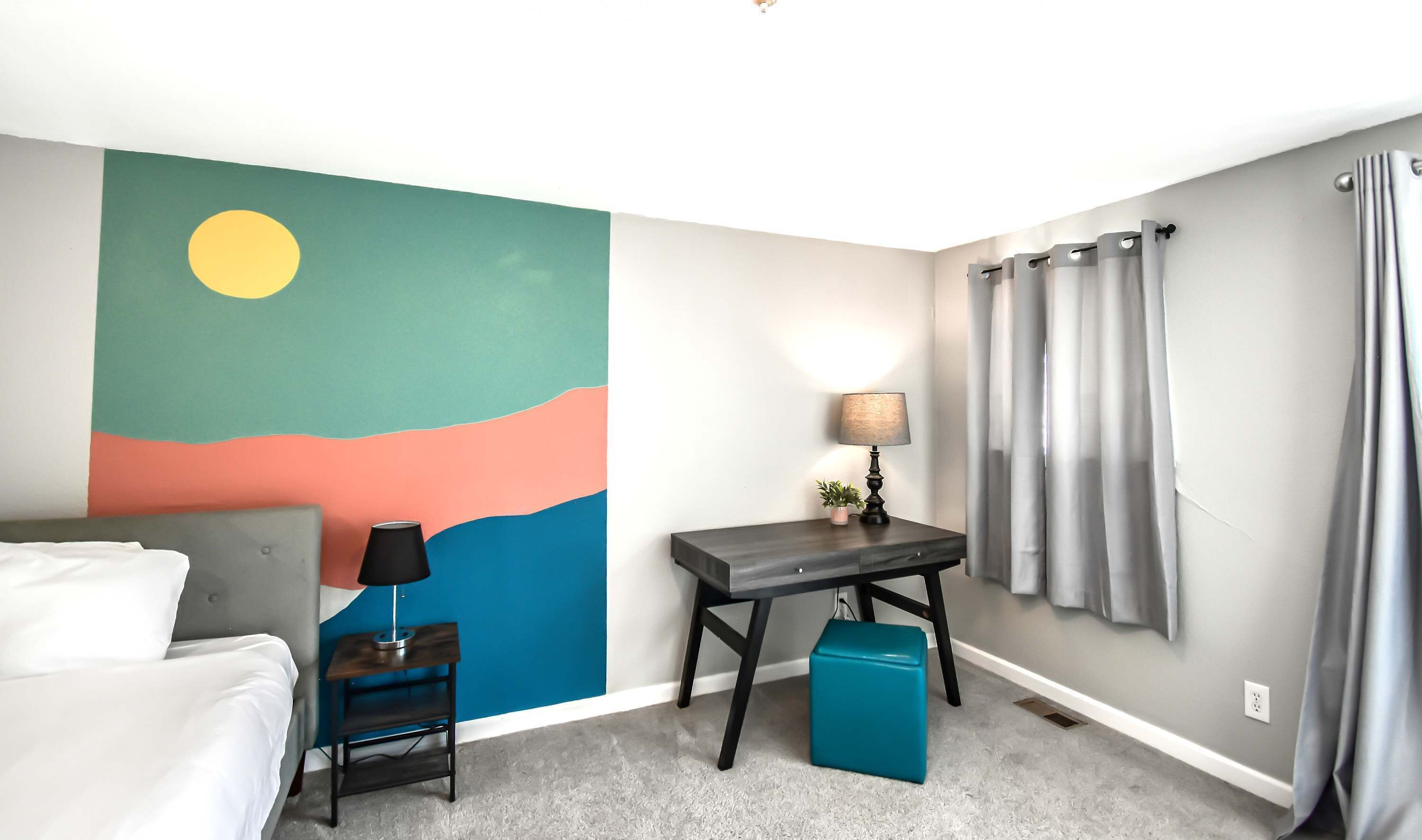A hotel room with a bed, a nightstand, a desk, a lamp, a small plant, and a window with curtains.