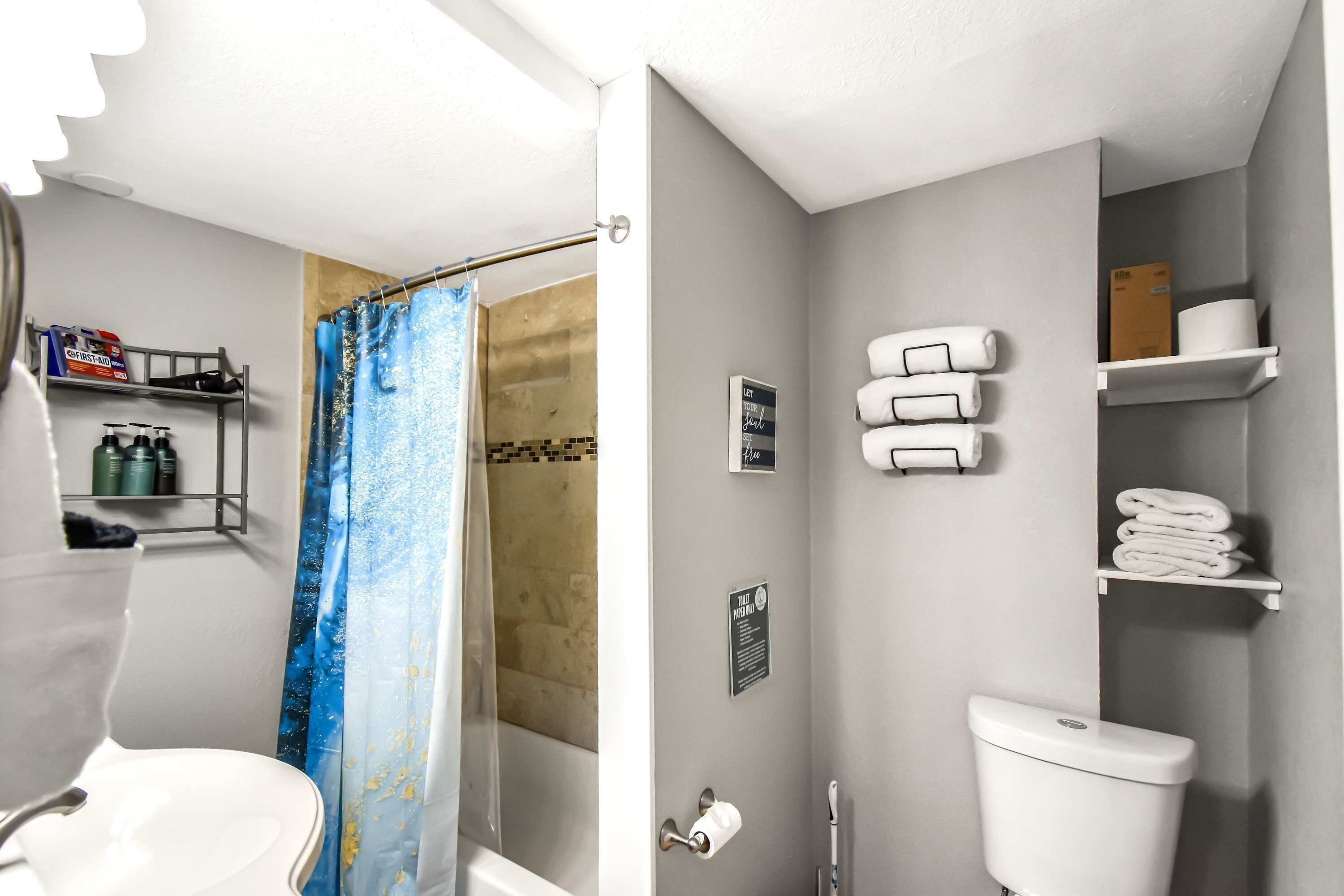 Ein Badezimmer mit Dusche, Toilette und Waschbecken. Handtücher und Toilettenartikel befinden sich in Regalen.