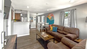 A modern living room with a brown leather sofa, a wooden coffee table, and a dining area with a white table and chairs. - Dog Friendly and Family Sized Home (Denver)