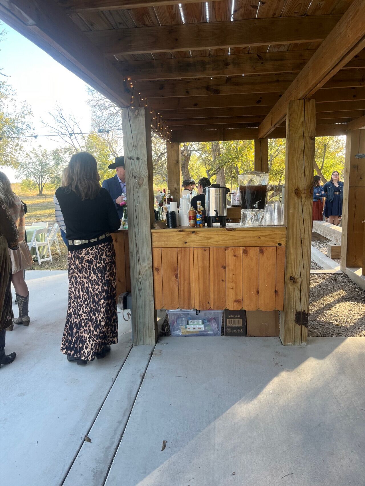 A wooden outdoor bar area with a counter, a coffee machine, and various bottles.