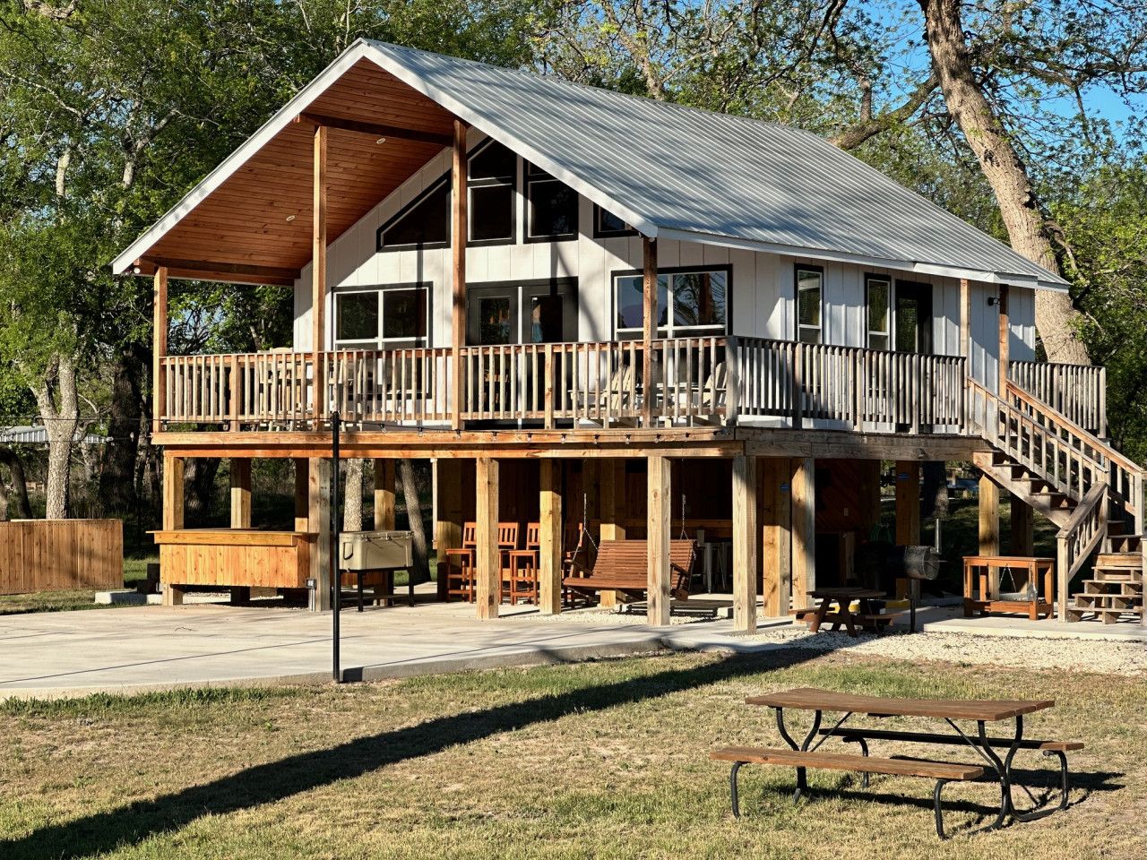 A two-story wooden cabin with a balcony, outdoor seating, and a picnic table.