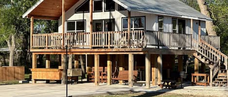 A two-story wooden cabin with a balcony, outdoor seating, and a picnic table.